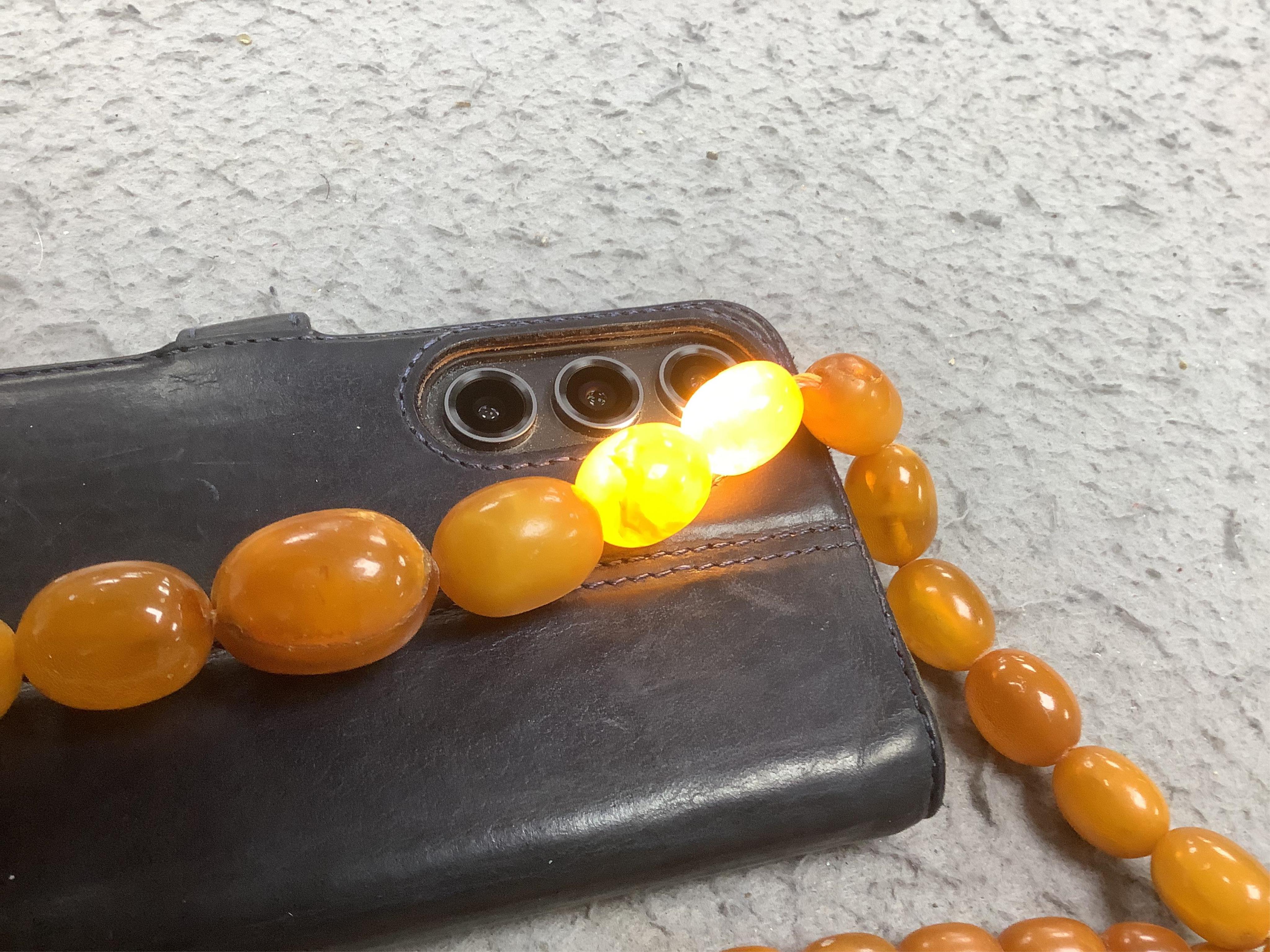 A single strand graduated oval amber bead necklace (a.f.), 90cm, gross weight 72 grams and three odd beads and an earring. Condition - poor